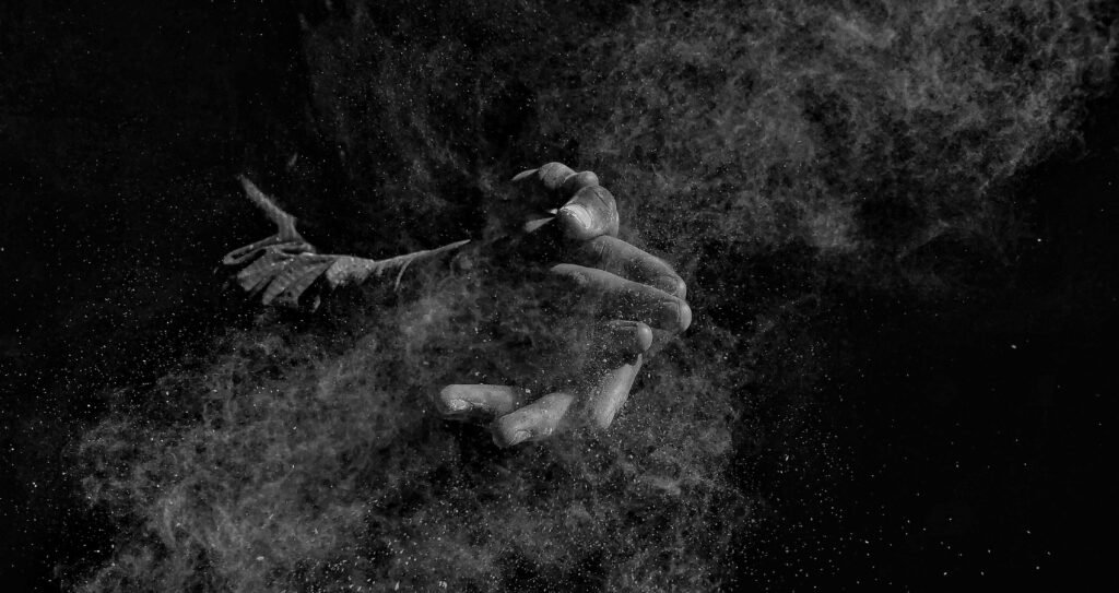 Artistic black and white image of hands clapping, creating a dramatic dust cloud.